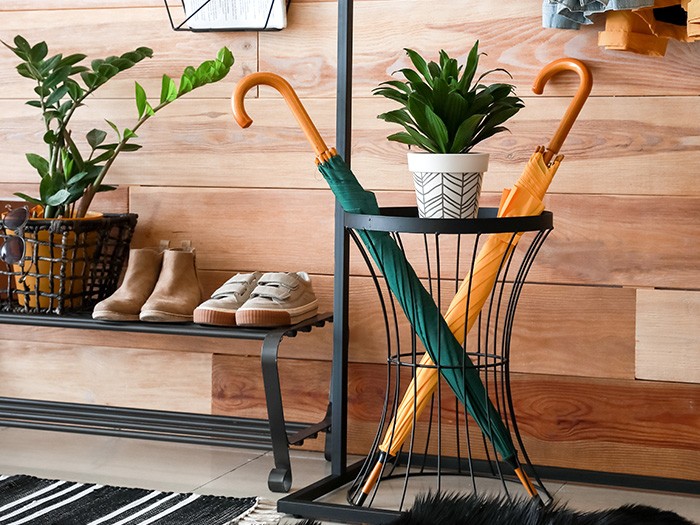Mudroom area with wooden wall, a bench with shows and a wire basket with a green and yellow umbrellas.